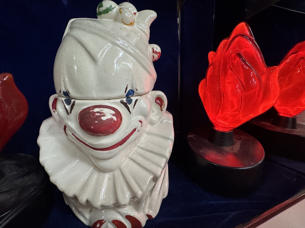 A ceramic clown jar beside red glass